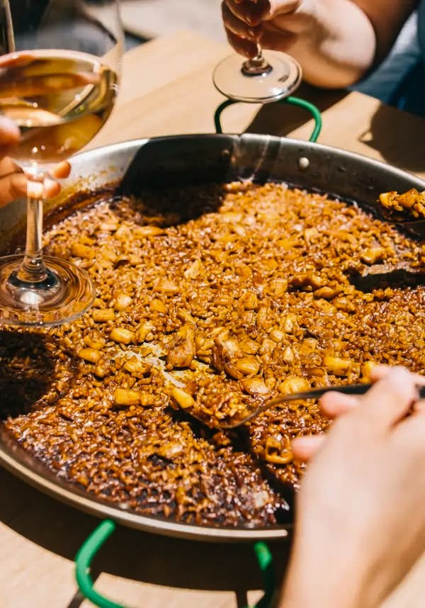 Hands and glasses around a wide pan of paella
